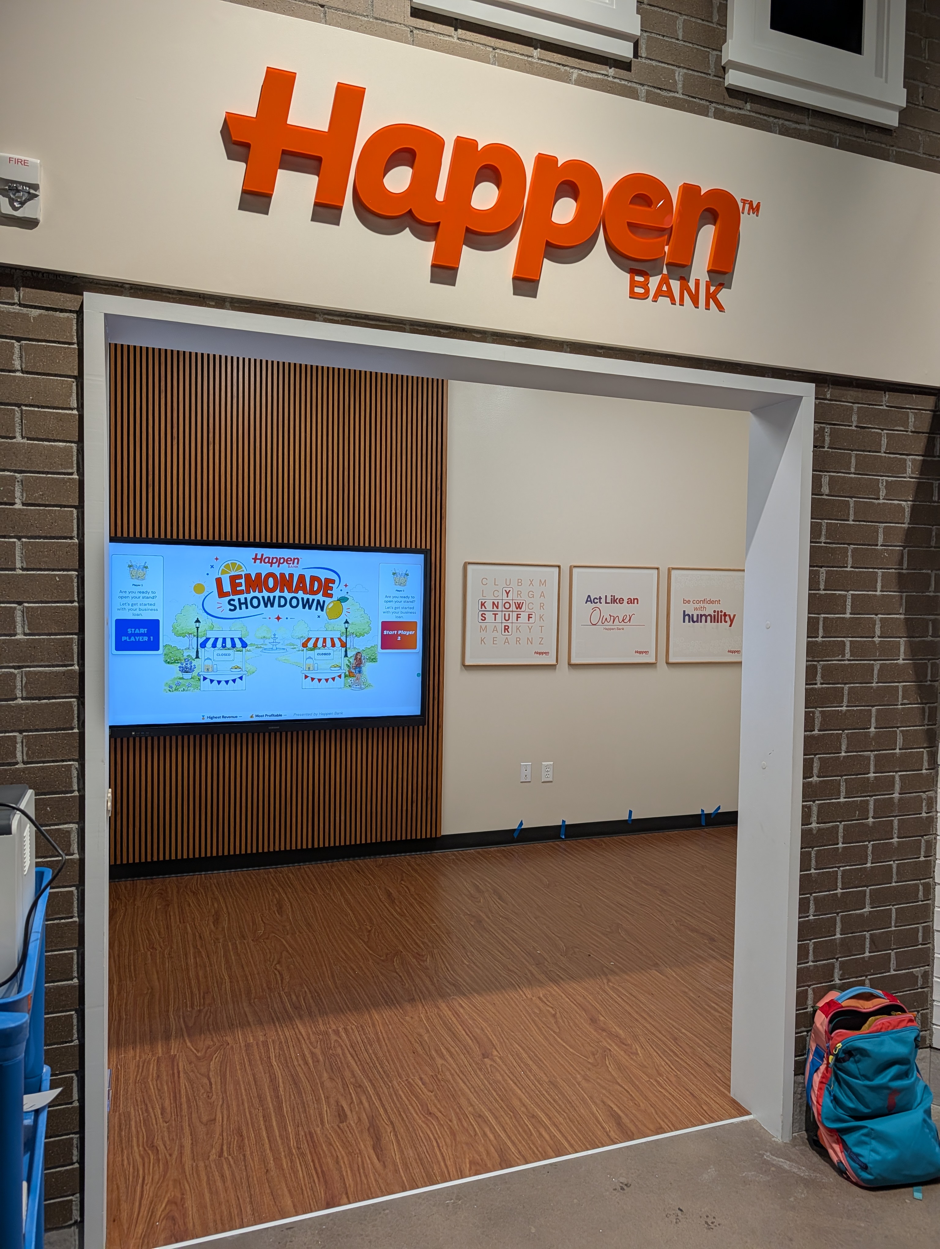 Lemonade Showdown on a large touchscreen inside the Happen Bank storefront, with the attract screen inviting Player 1 and Player 2 to start
