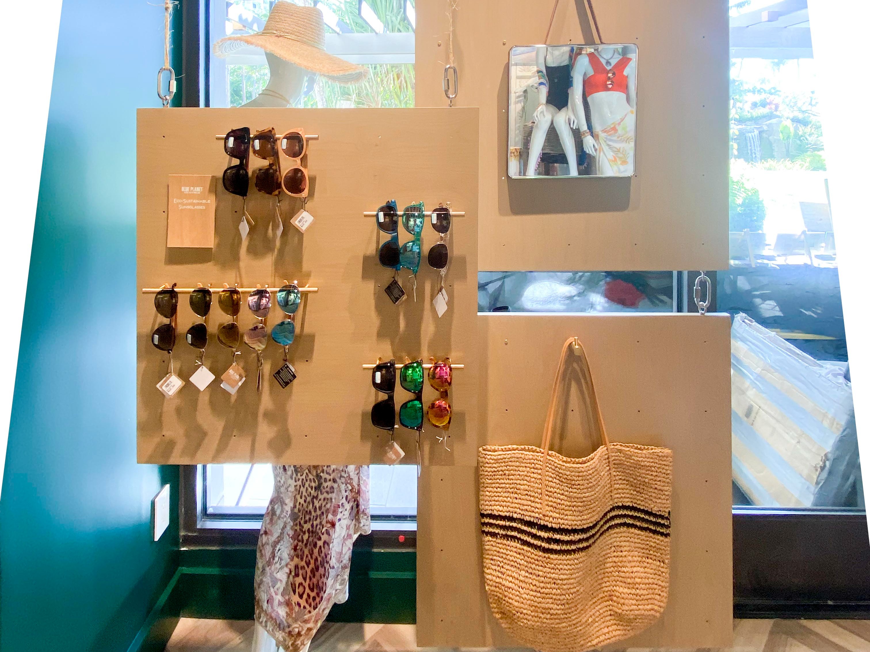 Suspended plywood panels float eco-sustainable sunglasses, totes, and beach hats by the window