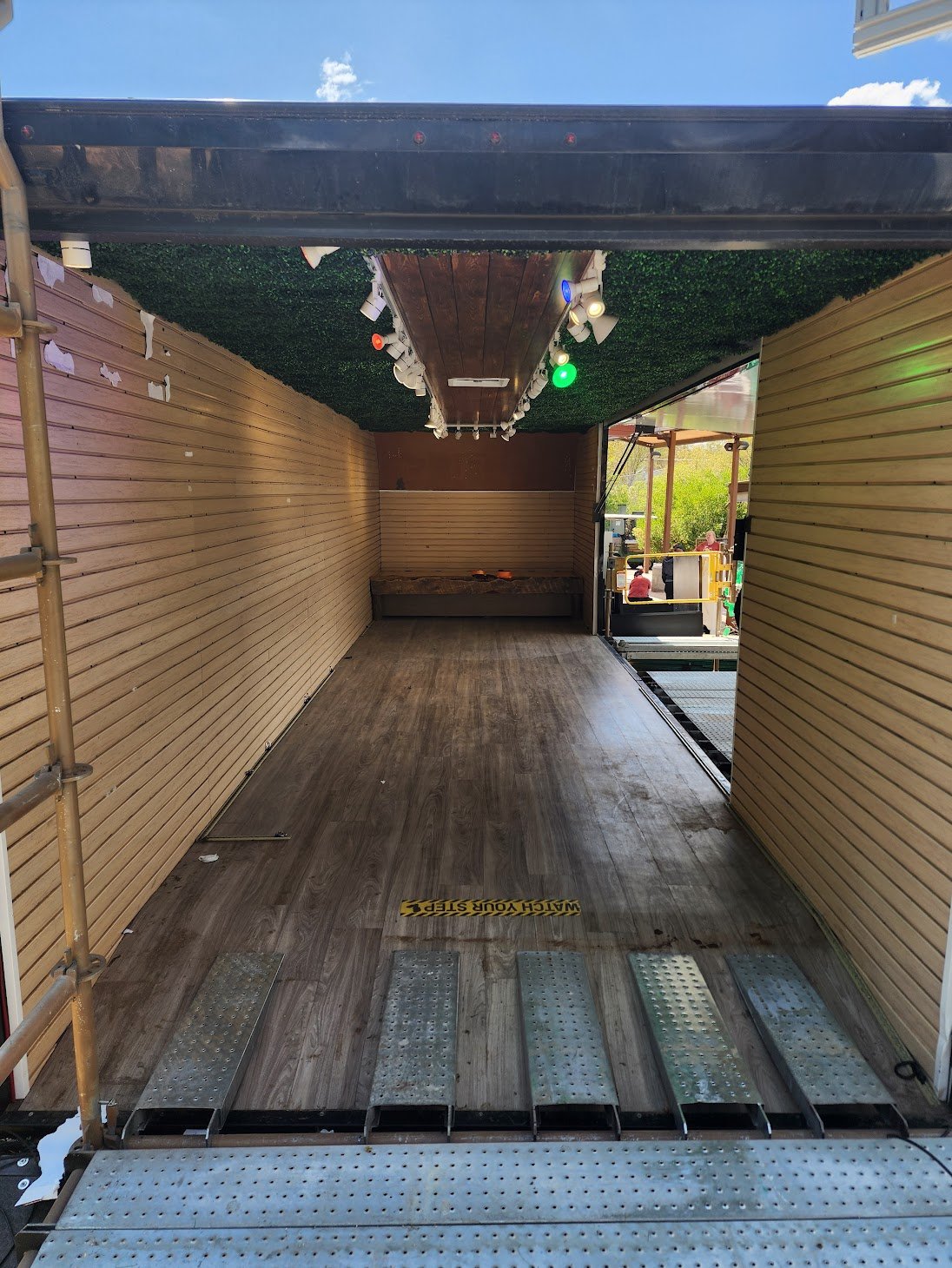 The 20-foot sidewall lifted into a canopy — wood-lined interior, track lighting, and a deployable ramp turn the trailer into an open-air room